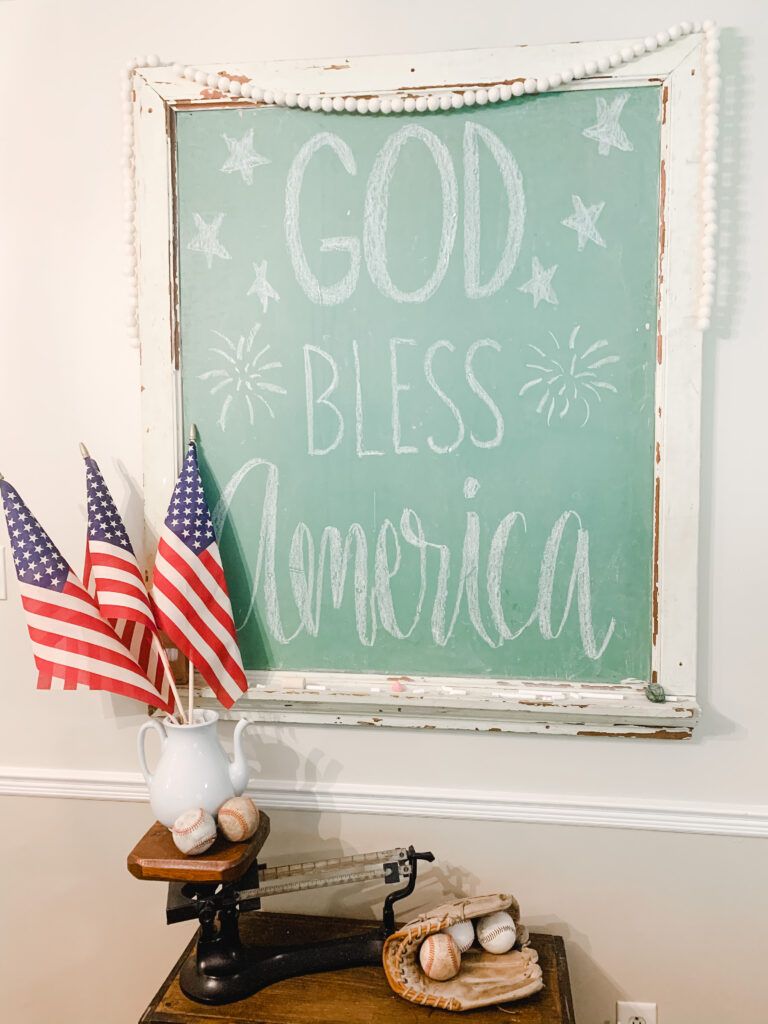 American flags and baseballs displayed in front of a chalkboard with "God Bless America."